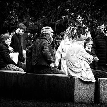 A small group of people sit on a stone seat in St Andrew Square, Edinburgh