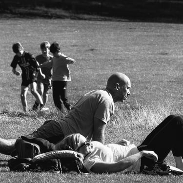 A woman sunbathes while behind her, a man does some stretching exercises on Bruntsfield Links, Edinburgh