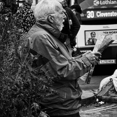 A rather puzzled looking man, holds a map as he leans against a flower bed. The High Street by North Bridge, Edinburgh