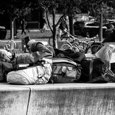 A backpacker, on his phone, takes it easy, lounging on a stone bench outside The Scottish Parliament, Edinburgh