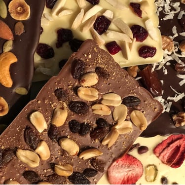 Handcrafted gourmet chocolate bars topped with dried fruits and nuts, elegantly arranged for gifting or indulgence.