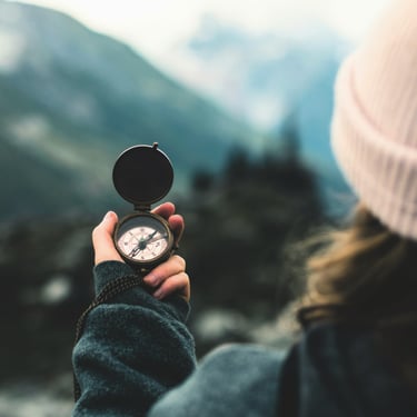 woman's hand holding compass in front of blurry nature backdrop