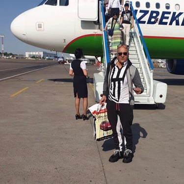 a man in a jacket and sunglasses is in front of Uzbekistan Airways Plane