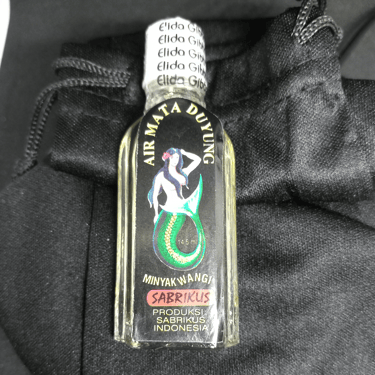 a bottle of oil on a black velvet drawstring bag
