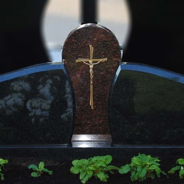 trijų dalių juodo akmens paminklas su rudu kryžiumi per vidurį