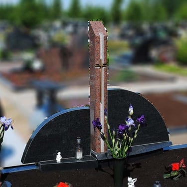 trijų dalių juodo akmens paminklas su rudu kryžiumi per vidurį