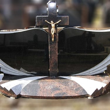 trijų dalių juodo akmens paminklas su rudu kryžiumi per vidurį