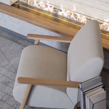 Cozy living area with light armchair, wooden armrests, sleek fireplace, and small side table in modern design.
