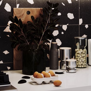 Modern kitchen with sqaure wall tiles, black vase, green leaves, cutting board, eggs, and minimalist design.