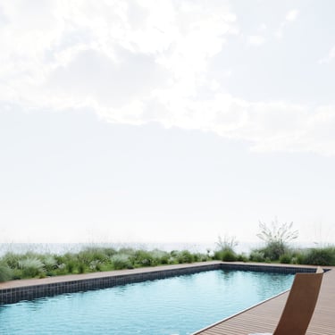 3D rendering of modern outdoor scene with clear pool, wooden deck, lush greenery, natural light, and partly cloudy sky.