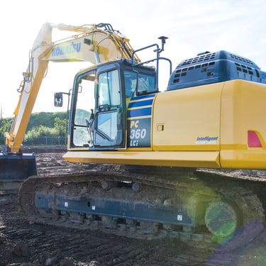 A heavy equipment technician is seen approaching a Komatsu PC360LCi smart construction excavator.