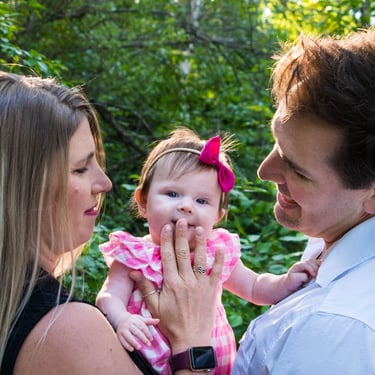 A happy couple holding the child and gazing at her. The child glances at the camera, smiling slightly. 