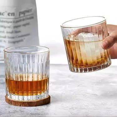 a person holding a glass of alcohol in front of a bottle of alcohol