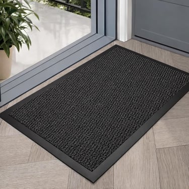 Durable black non-slip indoor outdoor doormat on a herringbone floor by a glass doorway.