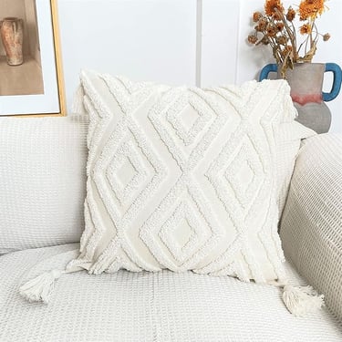 White boho tufted throw pillow with textured diamond pattern and corner tassels on a neutral sofa.