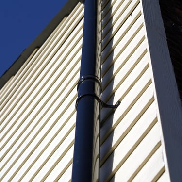 White cladded house wall with black guttering and downpipe
