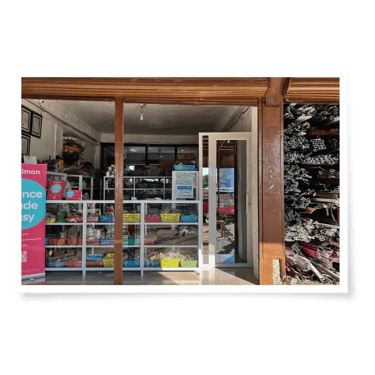 A view of a hardware store entrance with shelves of colorful supplies and metal materials stacked outside. Sunlight brightens