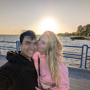 Introduction image of Lennard and Anne on a pier at sunset. The woman kisses the smiling man 