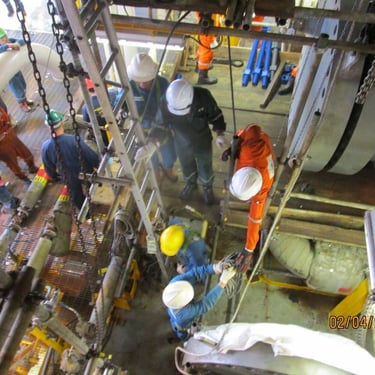 Offshore oil rig workers performing heavy industrial maintenance and equipment inspection on a metal platform.