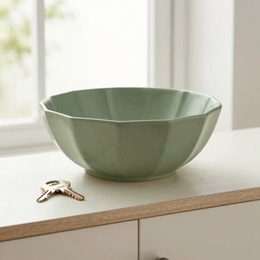 Sage green faceted decorative bowl holding fresh keys on an entryway console table, bright daytime lighting