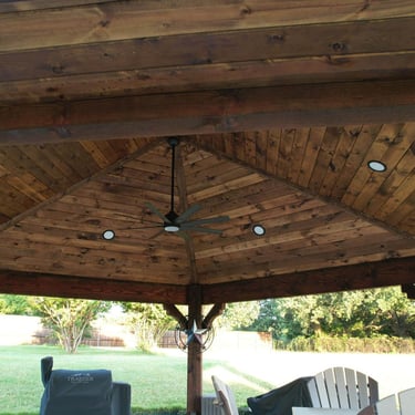 Wooden gazebo ceiling with fan and recessed lighting.