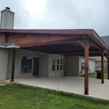 Covered backyard patio with wooden beams and concrete flooring.