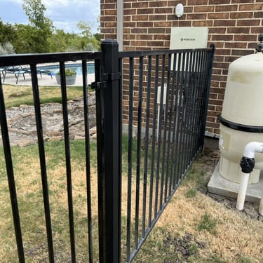 Black metal pool fence gate near filtration system.