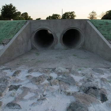 Concrete twin-pipe culvert with rock drainage.