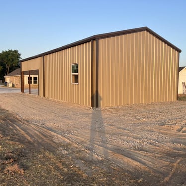 New tan metal shed with gravel driveway.