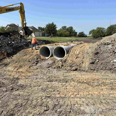 Installation of twin concrete drainage pipes with excavator.