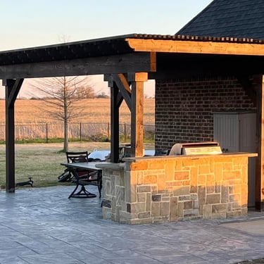 Covered outdoor kitchen with stone bar on stamped concrete patio.