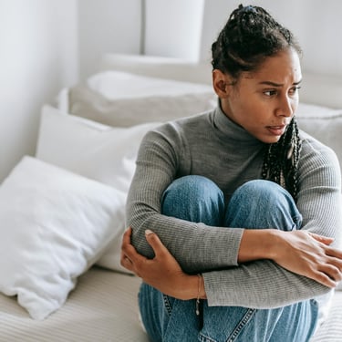 Concerned young woman sitting on a bed hugging her knees, reflecting mental health and anxiety.