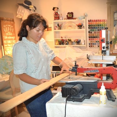 A young teenaged girl with ponytail cutting a wooden board with a machine