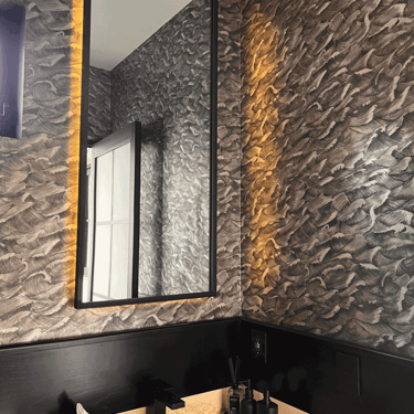 Detalle de baño decorado con papel tapiz texturizado e iluminación cálida indirecta en muro | KARÄNA
