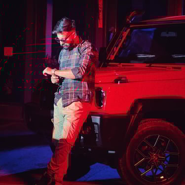 a man in a plaid shirt and jeans standing in front of a red car