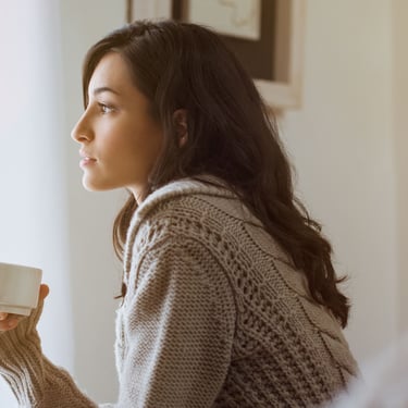 Anxious woman looking out window, looking forward to hypnotherapy session to regain confidence
