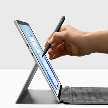 a person's hand holding a pen and writing on a laptop