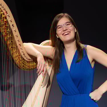 Clara Busemann steht lachen an einer Konzertharfe und hat einen Arm locker über ihre harfe gelegt