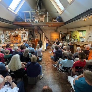 Clara Busemann sitzt in einem kleinen Konzertsaal. Ein Publikum hört ihr zu. der Raum ist voll mit menschen