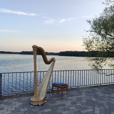 Eine Harfe steht an einem see mit sonnenuntergang im hintergrund. hinter der harfe steht eine türkiser hocker