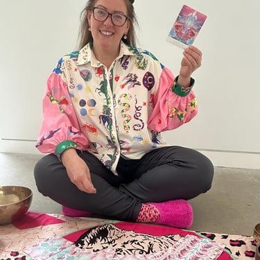 Gabi sitting on the floor holding an oracle card to welcome you to the leopard coven