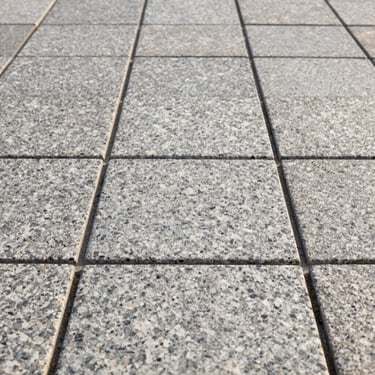 Close-up shot of perfectly aligned granite paving stones, crisp coastal morning light, showing high craftsmanship and clean lines