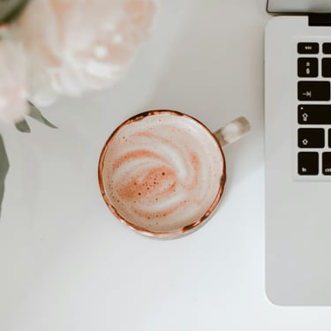 un espace bureau appaisant pourvu d'une tasse de café, des fleurs roses pales et un clavier d'ordinateur