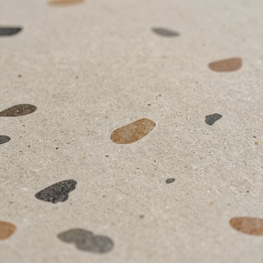 Macro close-up of natural terrazzo, warm grey base with embedded river pebble aggregates, polished matte finish.