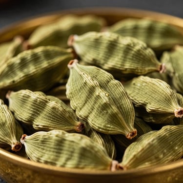 Macro close-up of textured green cardamom pods in a rustic brass bowl, dramatic side-lighting