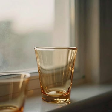 Close-up of vintage amber glassware catching soft golden-hour window light, warm editorial photography, 35mm film