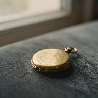 An antique brass locket showing natural wear on a dark velvet surface, soft focus, warm golden-hour light, 35mm film