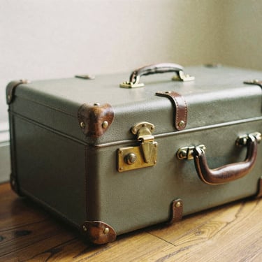 Warm editorial close-up of a vintage leather suitcase with brass clasps resting on a wooden floor, soft warm lighting, 35mm film