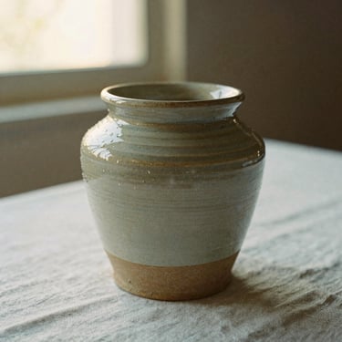 Aged ceramic stoneware crock jar sitting on a linen tablecloth, warm overcast light, shallow depth of field, 35mm film