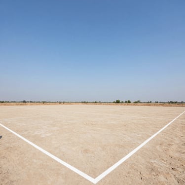 Wide environmental shot of a clean, cleared freehold land plot in Delhi NCR, marked boundaries under a clear blue sky, bright daylight, 35mm
